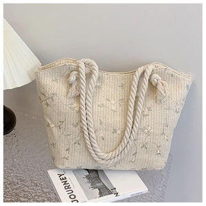 Close-up of woven straw tote bag featuring delicate floral embroidery and rope handles