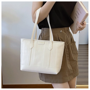 Close-up of white leather tote bag with fine wave texture and brand logo tag