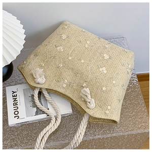 Detail of straw tote bag featuring floral embroidery and white cotton rope handle
