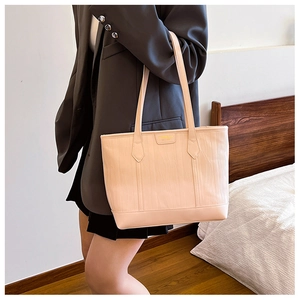 Detail of light pink textured tote bag with golden logo held by model in home setting