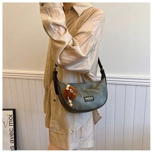 Detail of grey crescent shoulder bag with black leather trim and plush charm
