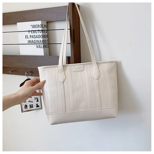 Détail d'un sac cabas crème en cuir synthétique avec texture ondulée et plaque logo metal