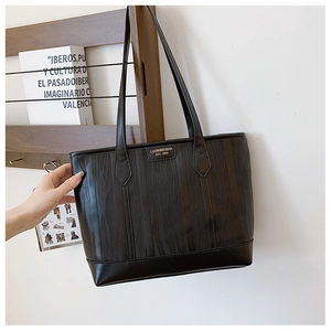 Détail du sac cabas noir avec texture ondulée unique et plaque de logo dorée élégante