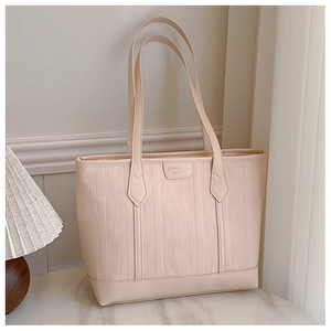 Detail of cream tote bag featuring wavy embossed texture and gold brand logo