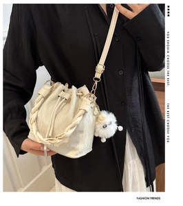Détail du sac seau crème avec poignée tressée et breloque en peluche sur le mannequin