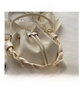 Détail macro du sac seau crème avec poignée tressée et anneau doré brillant