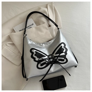 Detail of silver shoulder bag featuring a large black butterfly motif and lace-up details
