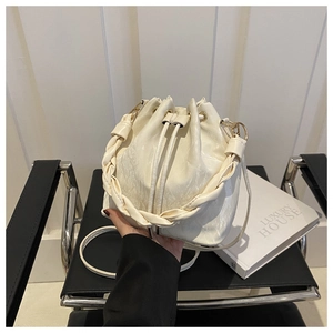 Détail du sac seau crème montrant la texture du cuir brillant et la poignée tissée