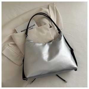 Close-up of a silver metallic hobo bag with a black shoulder strap on neutral fabric