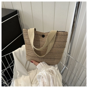 Détail du sac seau en paille kaki avec texture tressée et bouton rond noir décoratif