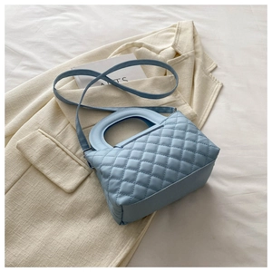 Détail du sac à main matelassé bleu clair avec motif losange sur fond de veste beige
