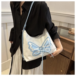 Close-up of white shoulder bag featuring light blue butterfly patch with lace-up detail