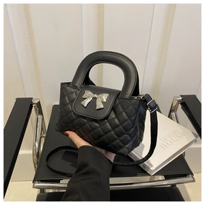 Détail du sac matelassé noir avec nœud argenté posé sur une chaise design moderne