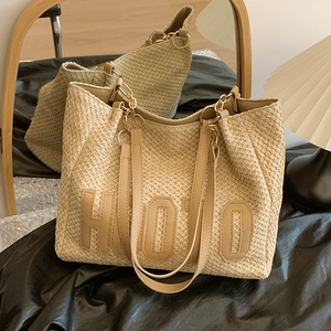 Large straw woven tote bag with HOJO lettering and leather straps in a cozy setting