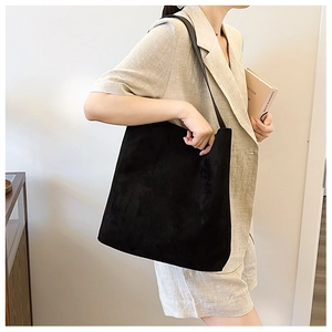 Dettaglio di una borsa tote in pelle scamosciata nera abbinata a un blazer beige