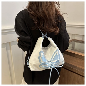 Détail d'un sac à dos en nylon blanc avec broderie papillon bleu clair et nœud ruban