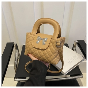 Détail du sac matelassé camel avec boucle nœud argenté sur un livre de luxe blanc