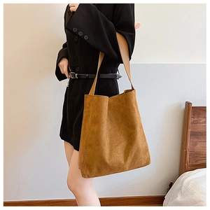 Dettaglio borsa tote in pelle scamosciata marrone con spalline in pelle su sfondo neutro