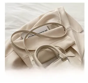 Détail du sac à bandoulière crème minimaliste montrant la poche zippée sur un blazer