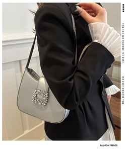 Close-up of silver underarm bag featuring a large square crystal buckle and metallic finish