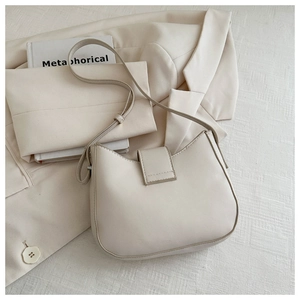 Close-up of minimalist cream half-moon shoulder bag with matte leather texture on a blazer