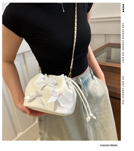 Detail showing white pleated drawstring bucket bag with satin bows and chain strap