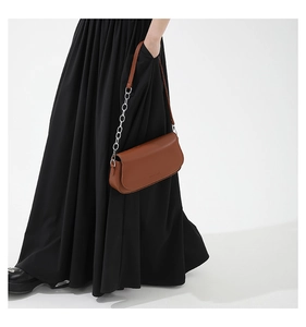 Close-up of brown leather saddle bag with silver metal chain strap on a black skirt