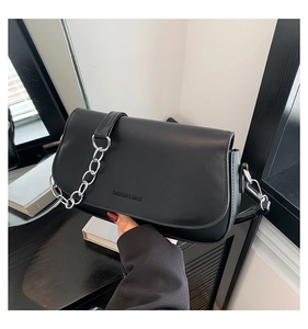 Detail of black saddle bag featuring embossed letters and silver metal chain strap