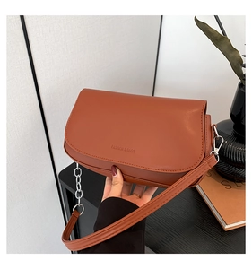 Detail view of brick red saddle bag featuring silver chain strap and fashion logo