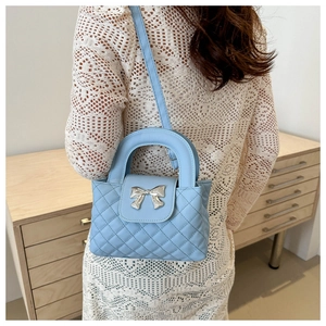 Sac à main bleu clair matelassé avec nœud argenté porté par un mannequin au style élégant
