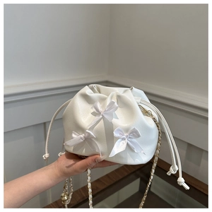 Detail showing white pleated bucket bag with satin bows and gold chain strap