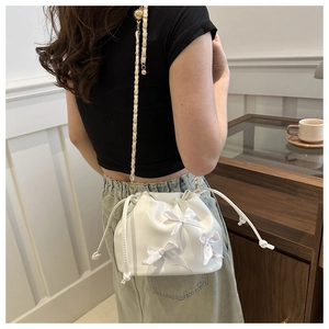 Détail du sac seau blanc à cordon avec nœuds en satin et bandoulière en chaîne dorée