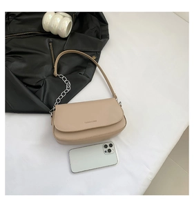 Detail of beige saddle bag showing matte leather texture, chain strap, and size comparison