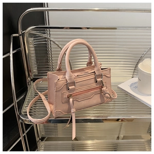 Détail du sac carré rose clair avec des pompons et des accessoires en métal argenté
