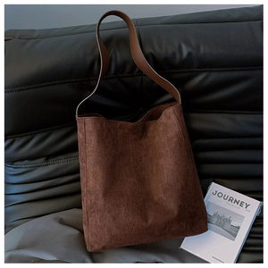 Dettaglio di borsa tote in pelle scamosciata marrone scuro su un divano in pelle nera