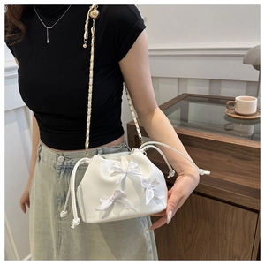 Detail of white bucket bag featuring elegant silk bows and gold-tone chain strap