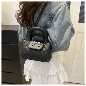 Close-up of black quilted crossbody bag featuring a silver metal bow buckle on a model
