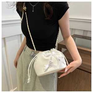 Detailed view of a white drawstring bucket bag with satin bows and a gold chain strap
