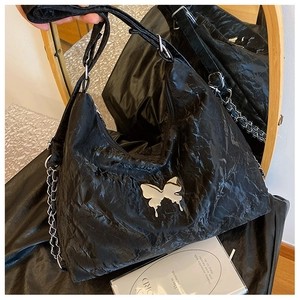 Close-up of black glossy PU shoulder bag with silver butterfly metal ornament and chain