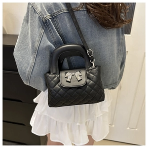 Sac matelassé noir avec nœud argenté porté en bandoulière sur jupe blanche