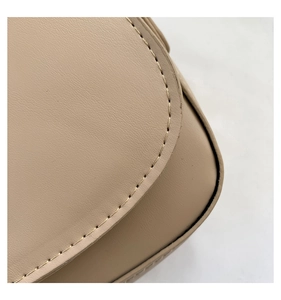Detailed close-up of fine stitching and smooth leather texture on an ivory saddle bag