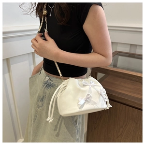 Detail of white drawstring bucket bag featuring satin bows and gold chain strap
