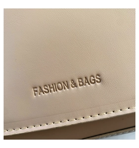 Close-up of beige leather saddle bag showing fine lychee texture and embossed fashion text