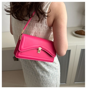 Detail of hot pink shoulder bag featuring wavy flap edge and gold metal clasp closure