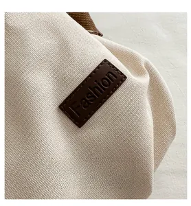 Detail of white canvas bucket bag with brown leather patch and embossed Fashion logo