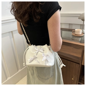 Detail of white drawstring bucket bag with satin bows and leather chain strap