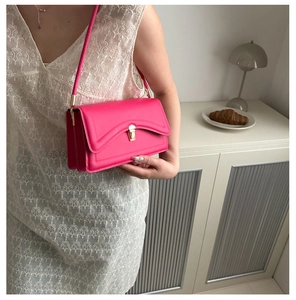 Detail of rose pink handbag featuring wave stitching and gold clasp on a model