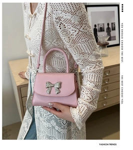 Detail of pink mini crossbody bag featuring a silver metal bow accent and leather handle