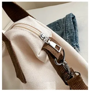 Close-up of smooth metal zipper and brown textured shoulder strap on canvas tote bag
