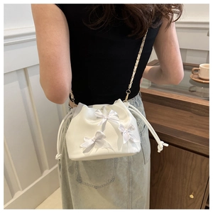 Détail du sac seau blanc avec nœuds décoratifs et bandoulière chaîne dorée